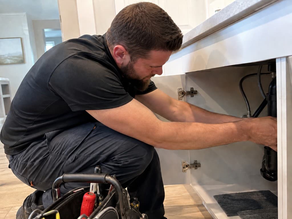 Flowline Plumbers technician repairing under-sink plumbing in a residential home